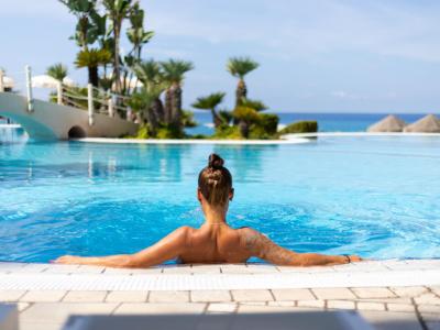 Donna rilassata in piscina con vista sul mare e palme.