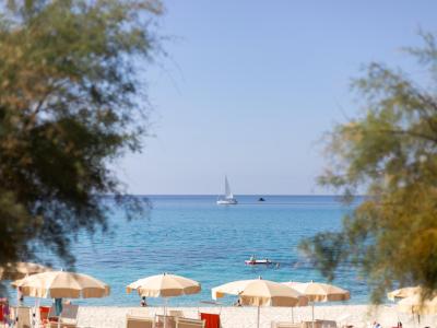 Spiaggia con ombrelloni, mare calmo e barca a vela all'orizzonte.