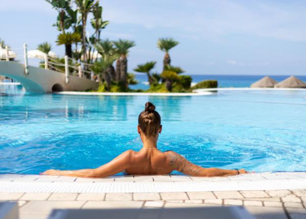 Donna rilassata in piscina con vista sul mare e palme.