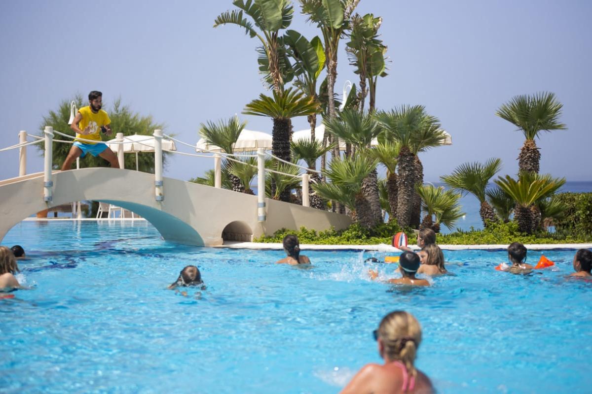 Piscina con animatore e persone che giocano in acqua sotto il sole.