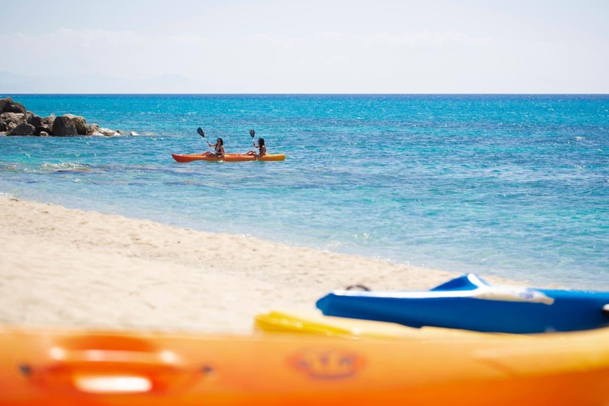 Due persone in kayak su un mare azzurro con spiaggia sabbiosa.