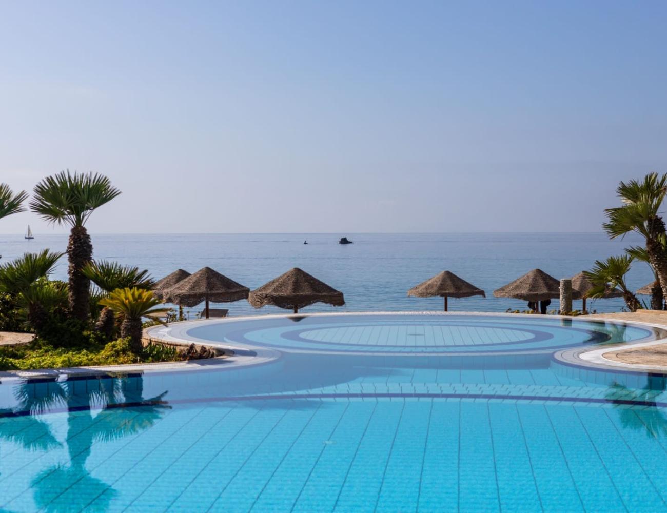 Piscine à débordement avec vue sur la mer et palmiers.