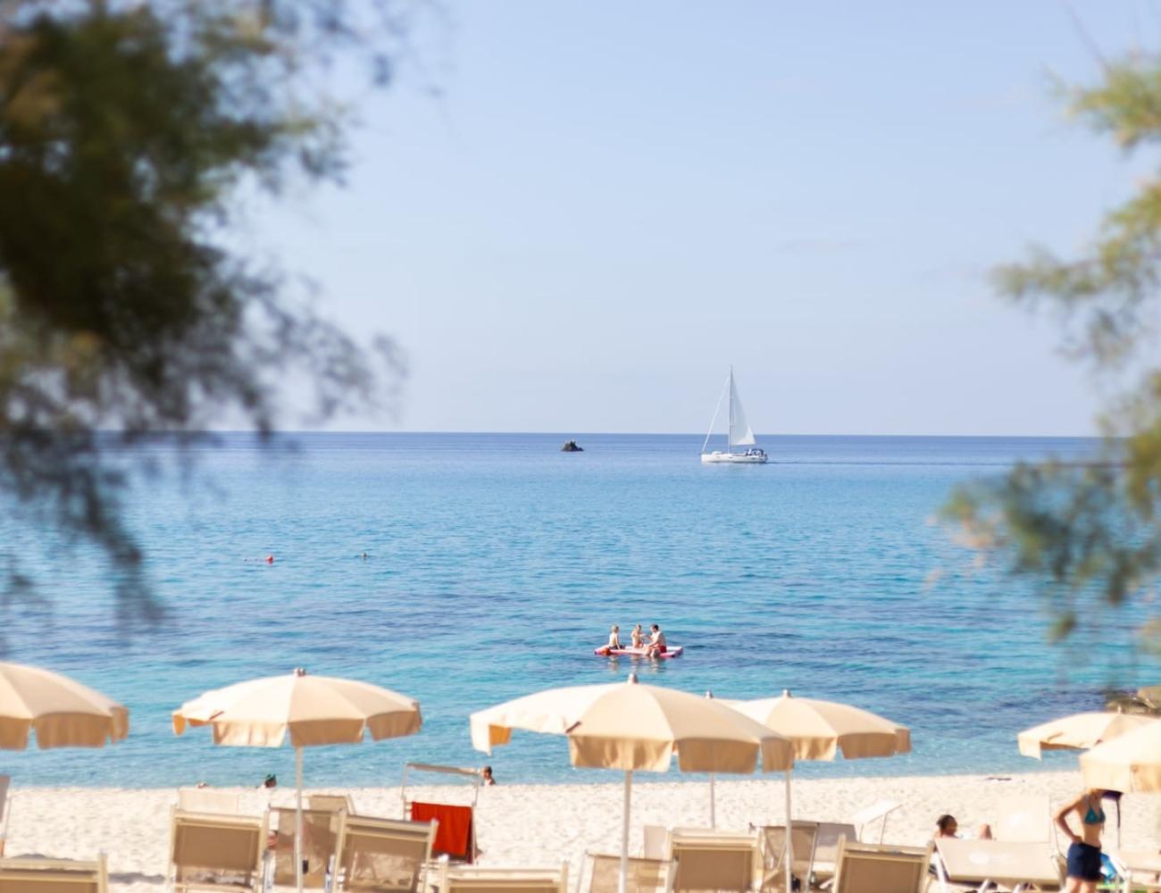 Plage avec parasols et voilier sur la mer.