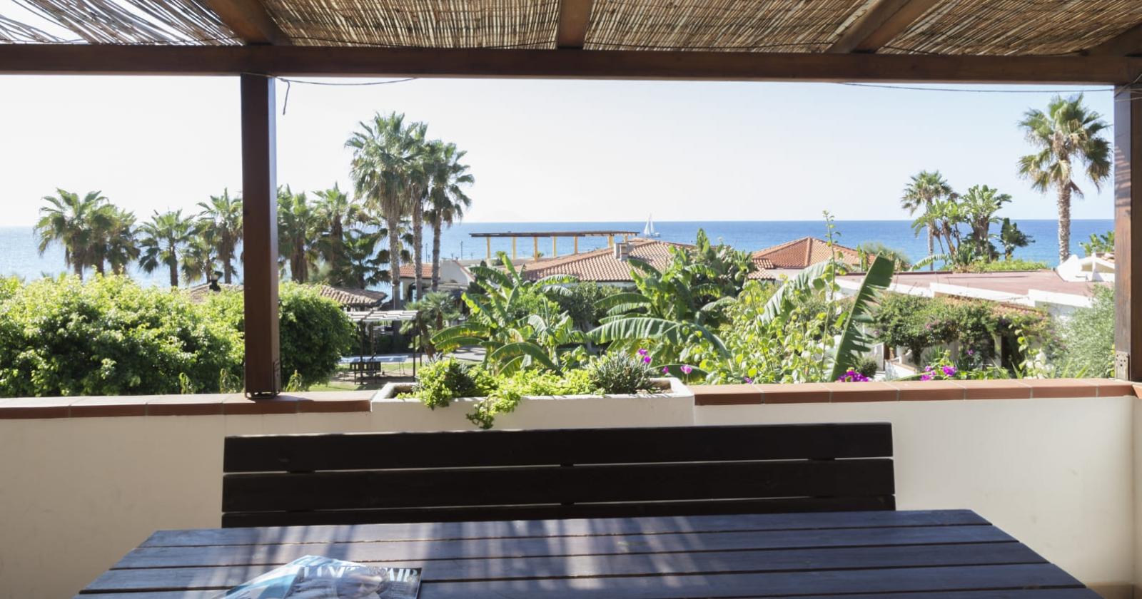 Vista mare da una terrazza con palme e vegetazione.