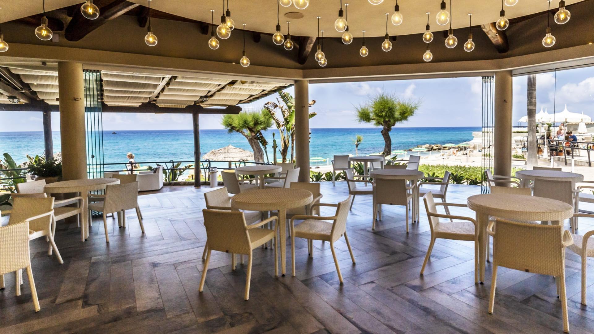 Ristorante con vista mare, arredamento moderno e luci sospese.