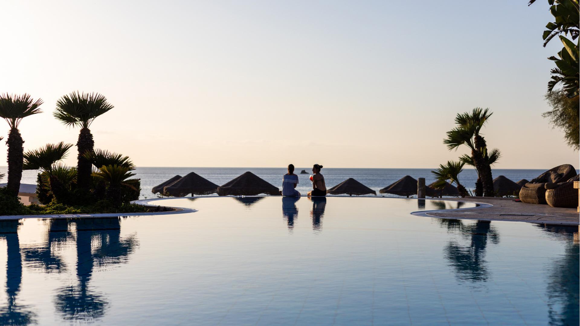 Due persone rilassate davanti alla piscina con vista mare.