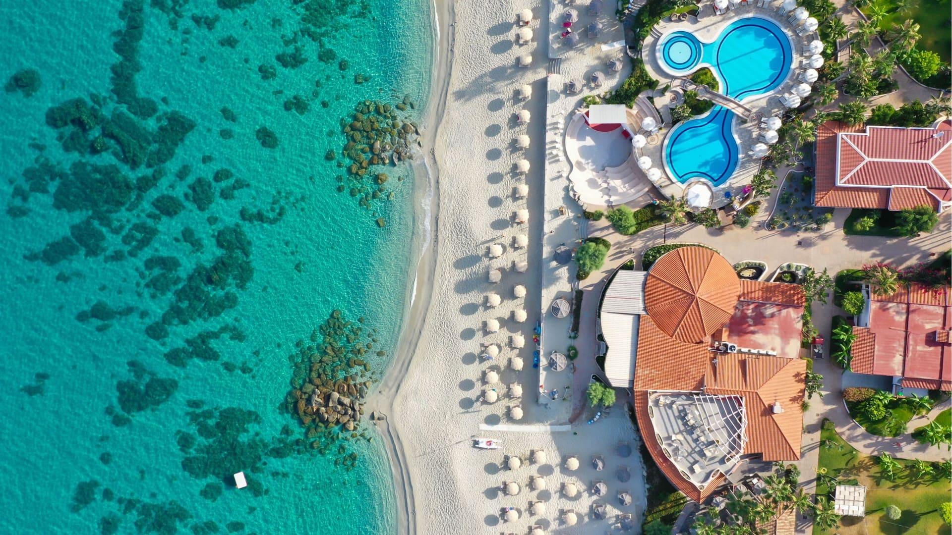 Beach with umbrellas, pool, and clear sea, aerial view.