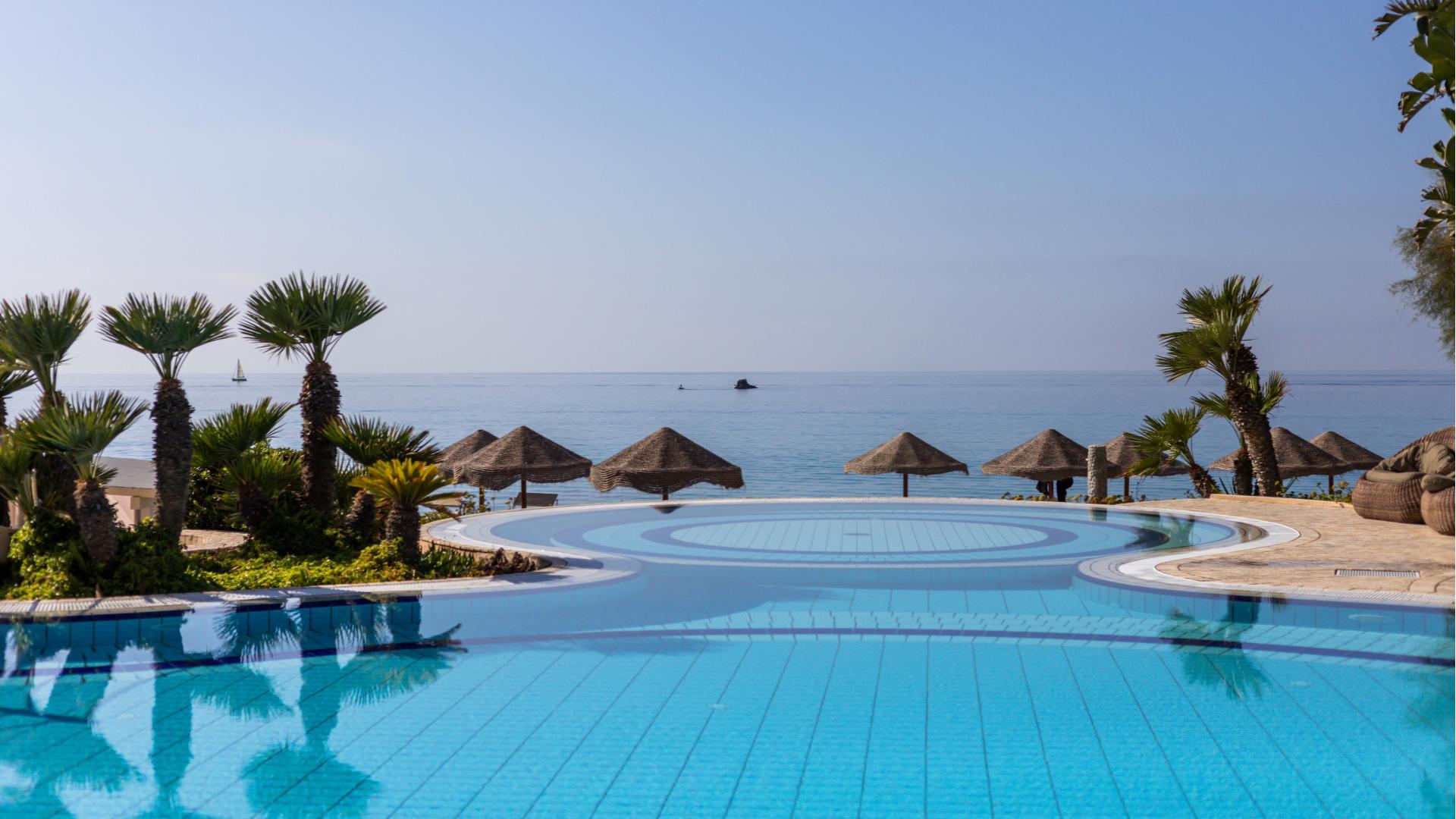 Piscina a sfioro con vista mare e palme.