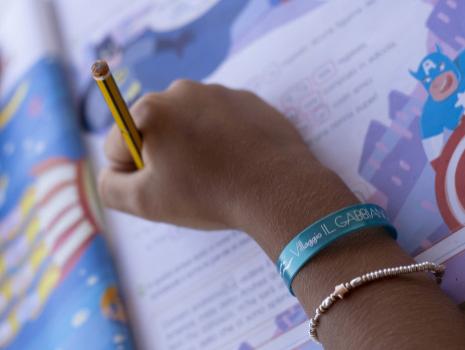 Hand with bracelet and pencil on colorful book.