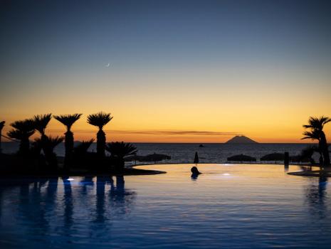 Sunset over the sea with palms and island on the horizon.