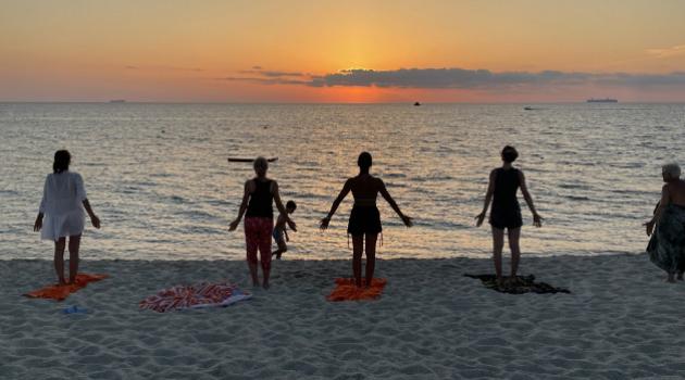 Persone fanno yoga sulla spiaggia al tramonto.