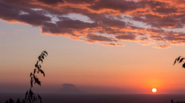 Sunset over the sea with clouds and a distant island.