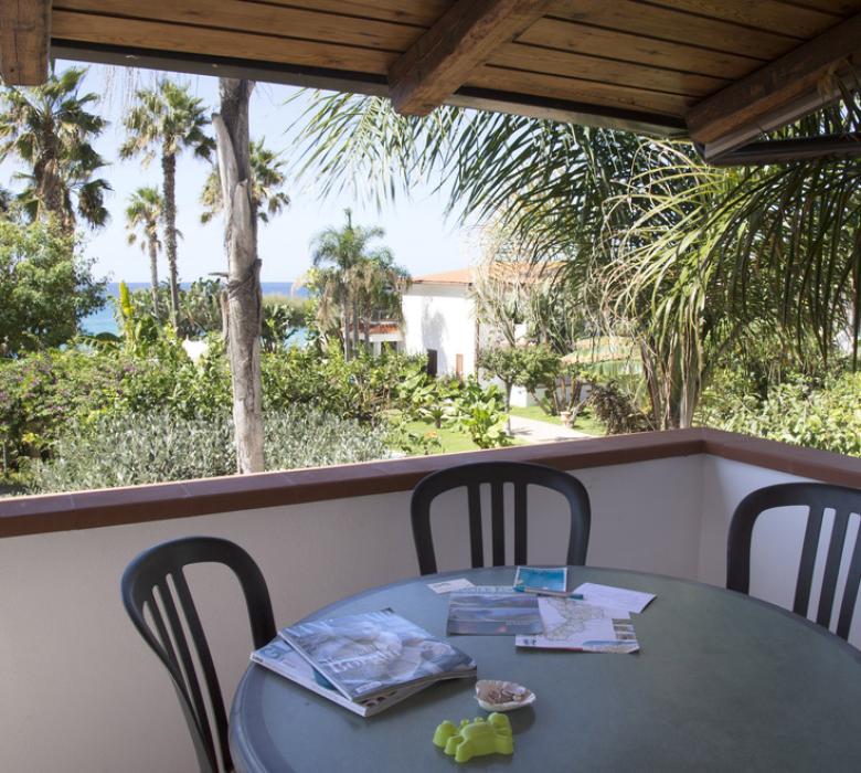 Terrazza con vista su giardino e mare, tavolo e sedie.