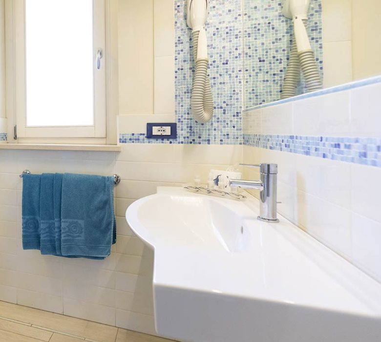 Bagno moderno con piastrelle blu, lavabo, bidet e asciugamani turchesi.