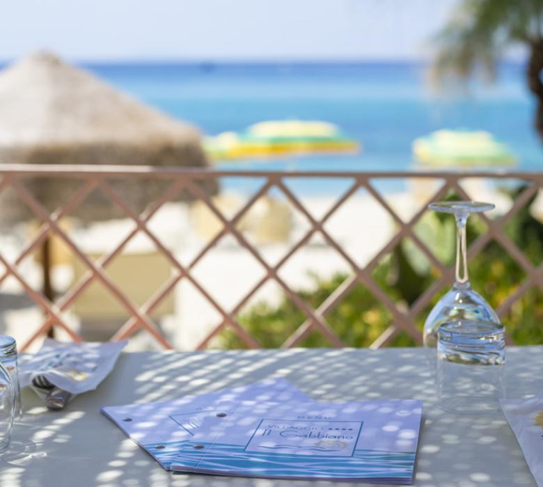 Tavolo vista mare con bicchieri capovolti e ombrelloni.