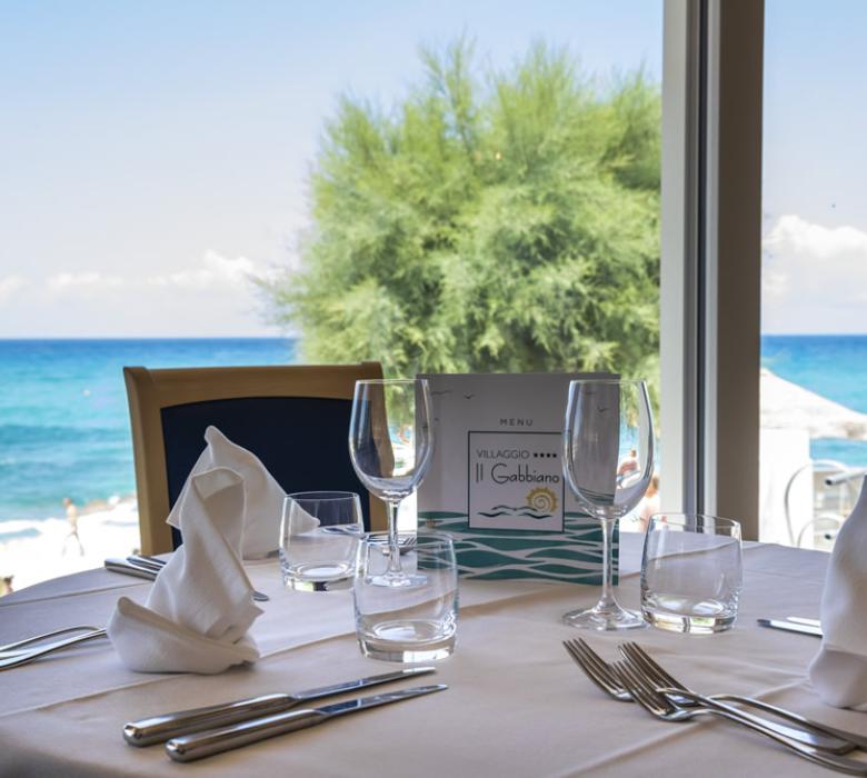 Tavolo apparecchiato con vista mare, ristorante Villaggio Il Gabbiano.