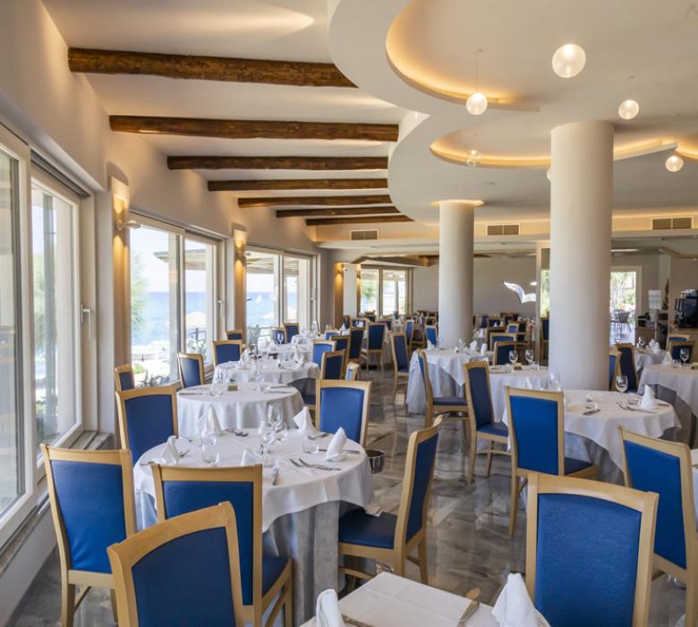 Ristorante elegante con vista mare, arredamento moderno e tavoli apparecchiati con cura.