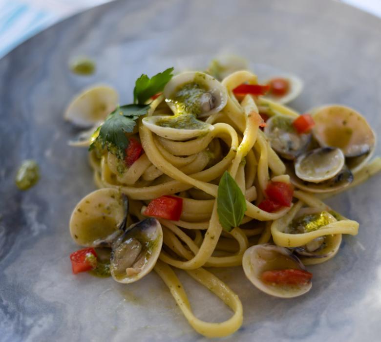 Linguine con vongole, pomodori e pesto su piatto elegante.