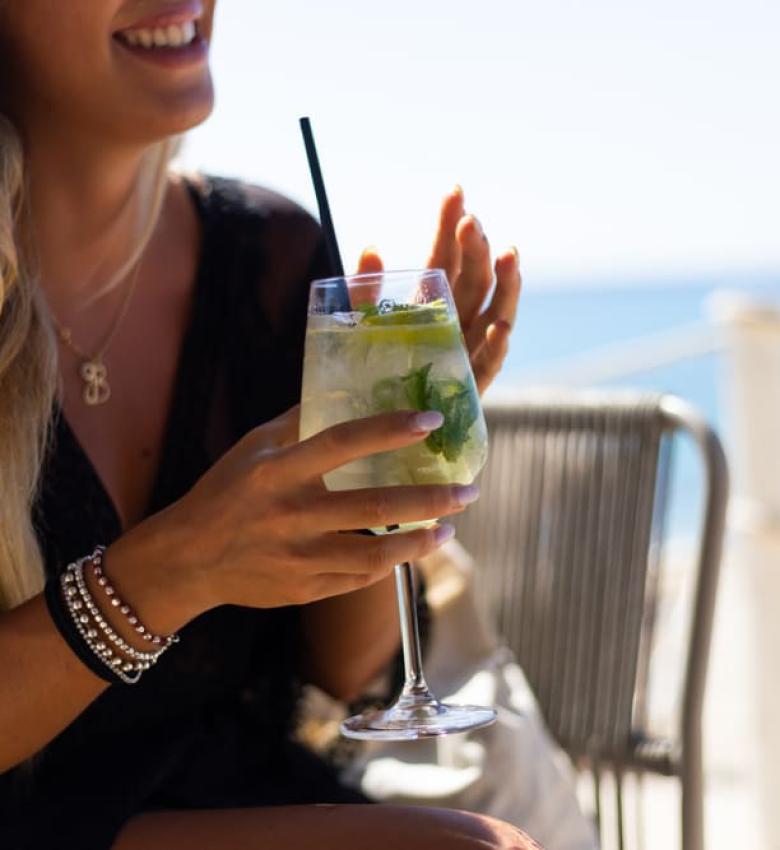 Donna sorridente con cocktail sulla spiaggia, giornata soleggiata.