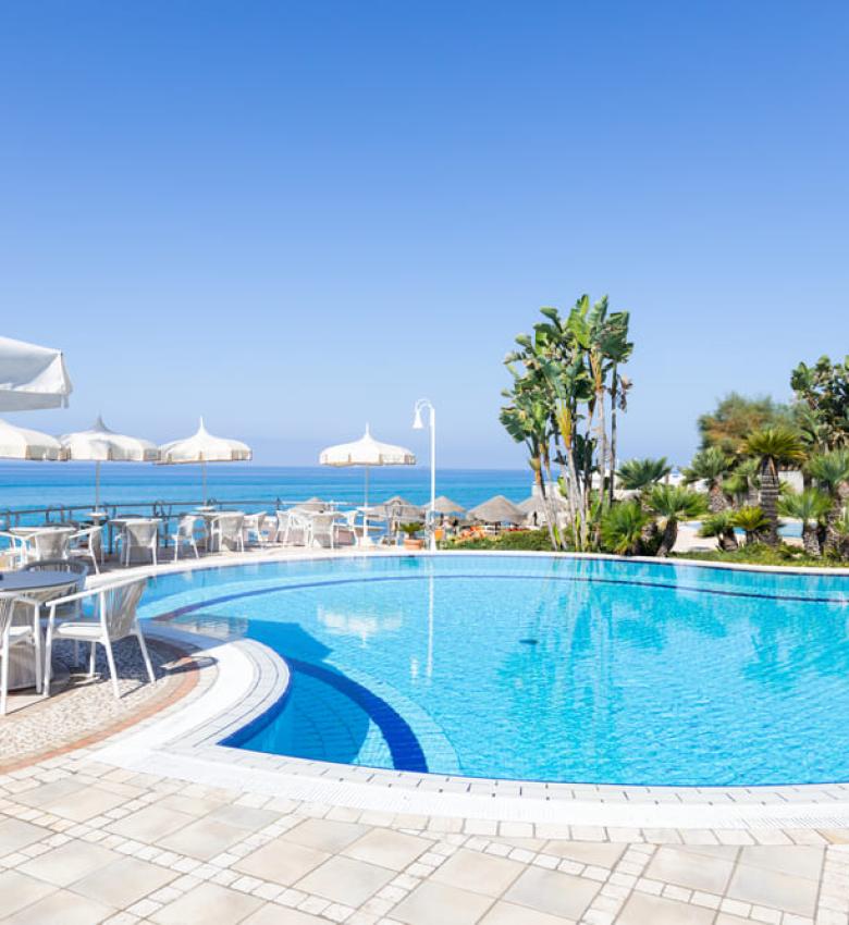 Piscina con vista mare, sedie e ombrelloni bianchi.