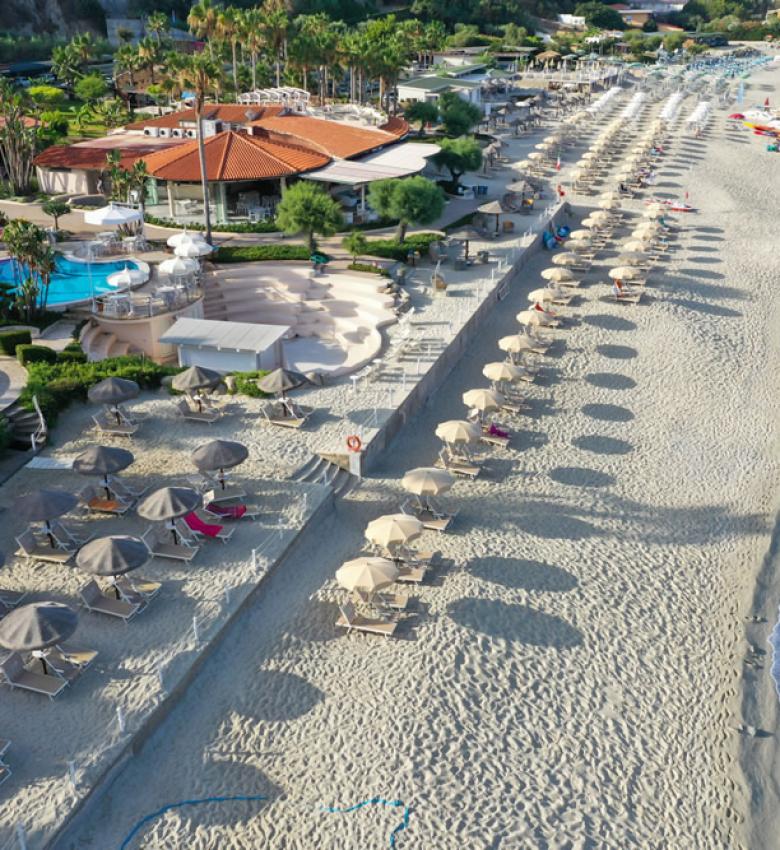 Spiaggia sabbiosa con ombrelloni, mare cristallino e piscina.