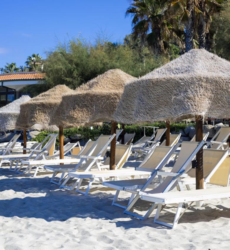 Spiaggia con lettini e ombrelloni di paglia, palme sullo sfondo.