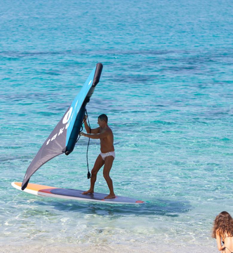 Uomo fa windsurf, due donne osservano in spiaggia.