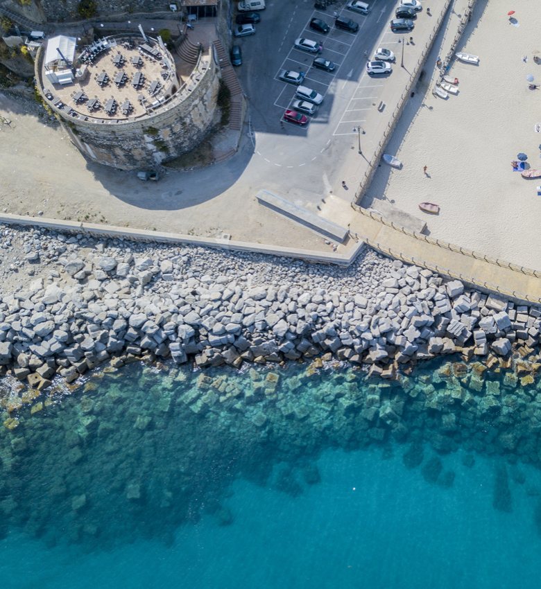 Vista aerea di una spiaggia, mare cristallino e una struttura circolare con tavoli.