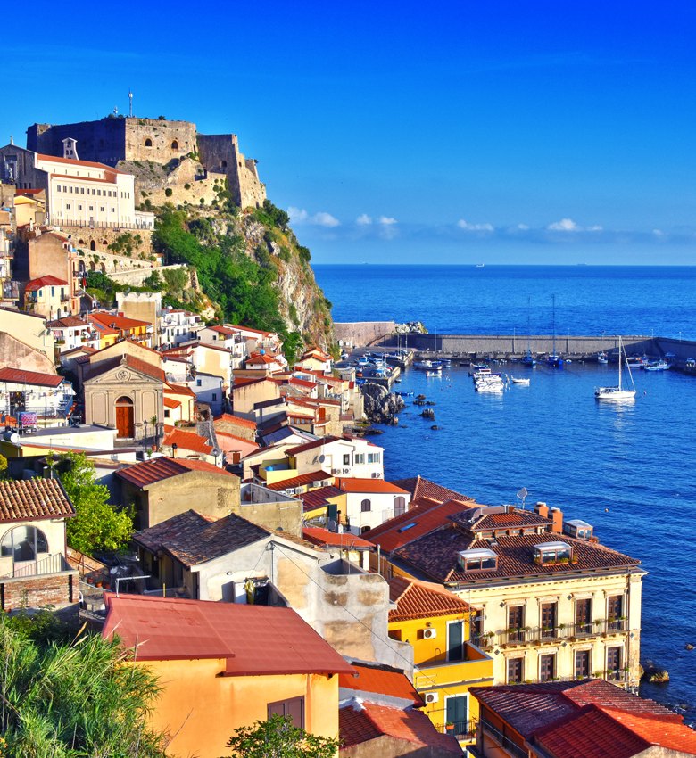 Vista sul mare con case colorate e un castello su una scogliera.