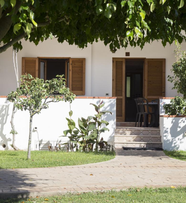 Casa bianca con giardino e veranda, circondata da alberi.