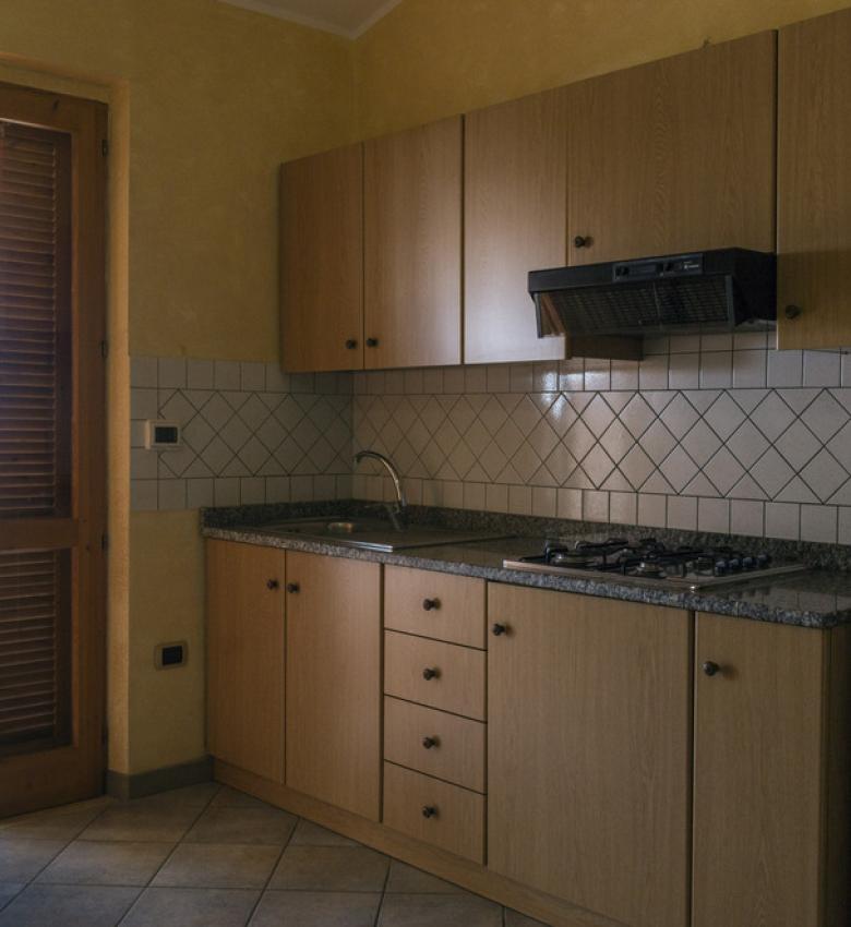 Cucina con mobili in legno e accesso al balcone.